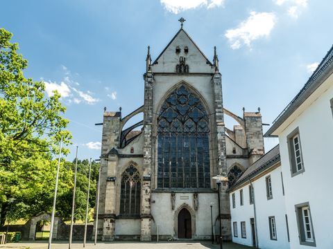 Zu sehen ist der Altenberger Dom in der Mitte des Bildes. Rechts sieht man Teile vom weißen Haus Altenberg, links steht ein grüner Baum.