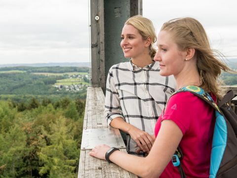 Zwei Frauen in Wanderkleidung stehen auf einem Aussichtsturm und blicken auf die weite Landschaft