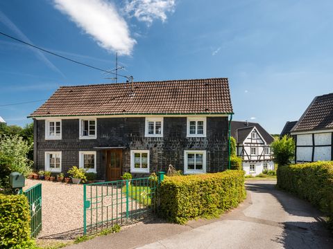 Ein Weg führt an einem alten Schiefenhaus vorbei, man sieht zwei Fachwerkhäuser