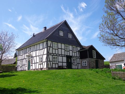 Auf iner grünen Wiese steht ein Fachwerkhaus mit verschiefertem Giebel, das von der Sonne angestrahlt wird.