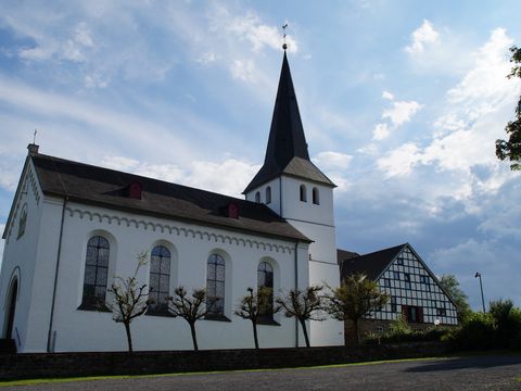 Weiße Kirche mit einem Turm neben einem Fachwerkhaus. 