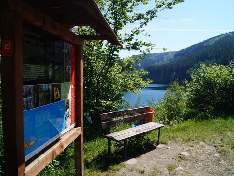 Infotafel mit einer Bank rechts daneben, dahinter die Aggertalsperre