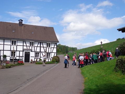 Eine Wandergruppe steht rechts neben einem Fachwerkhaus auf einer Straße und macht eine Pause. 