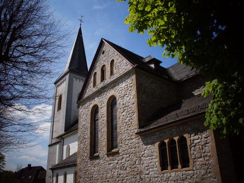 Kirche die einen weißen Turm hat und aus einem braun gemauerten Anbau besteht. 