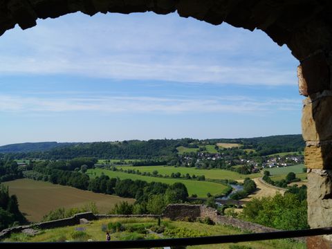 Blick durch ein gemauertes halbrundes Fenster auf weite Landschaft mit vielen Wiesen und Bäumen. 