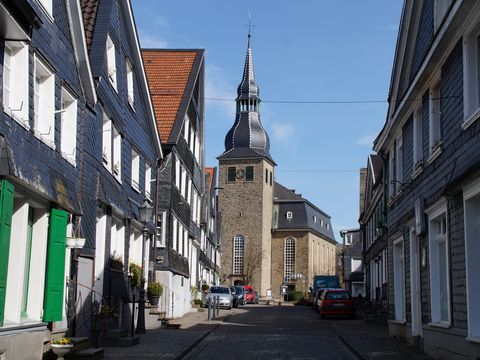 Blick durch eine mit verschieferten Wohngebäuden bebaute Straße bis zu einer Kirche.