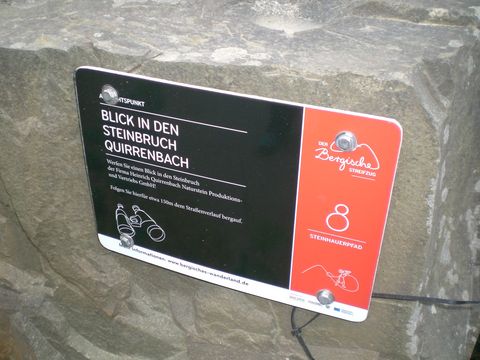An einem Grauwackestein ist eine Informationsplakette zum Steinhauerpfad angebracht.