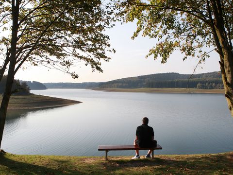 Eine Person die auf einer Bank am Ufer einer Talsperre sitzt wird von hinten fotografiert