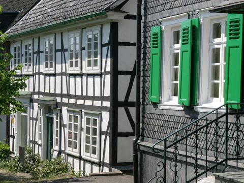 ein Schieferhaus mit grünen Fensterläden und ein Fachwerkhaus stehen direkt nebeneinander. 